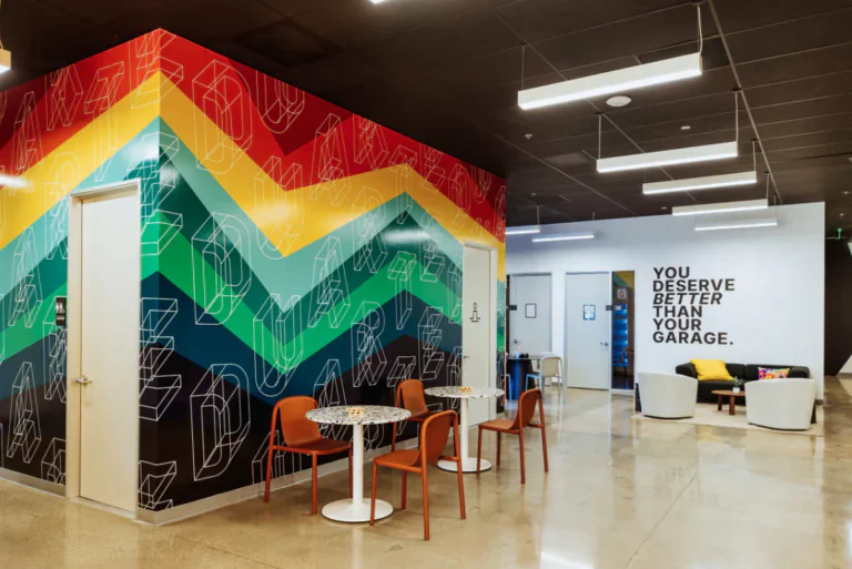 Colourful office interior with geometric wall art and a motivational quote. A small seating area with chairs and tables is in the foreground.
